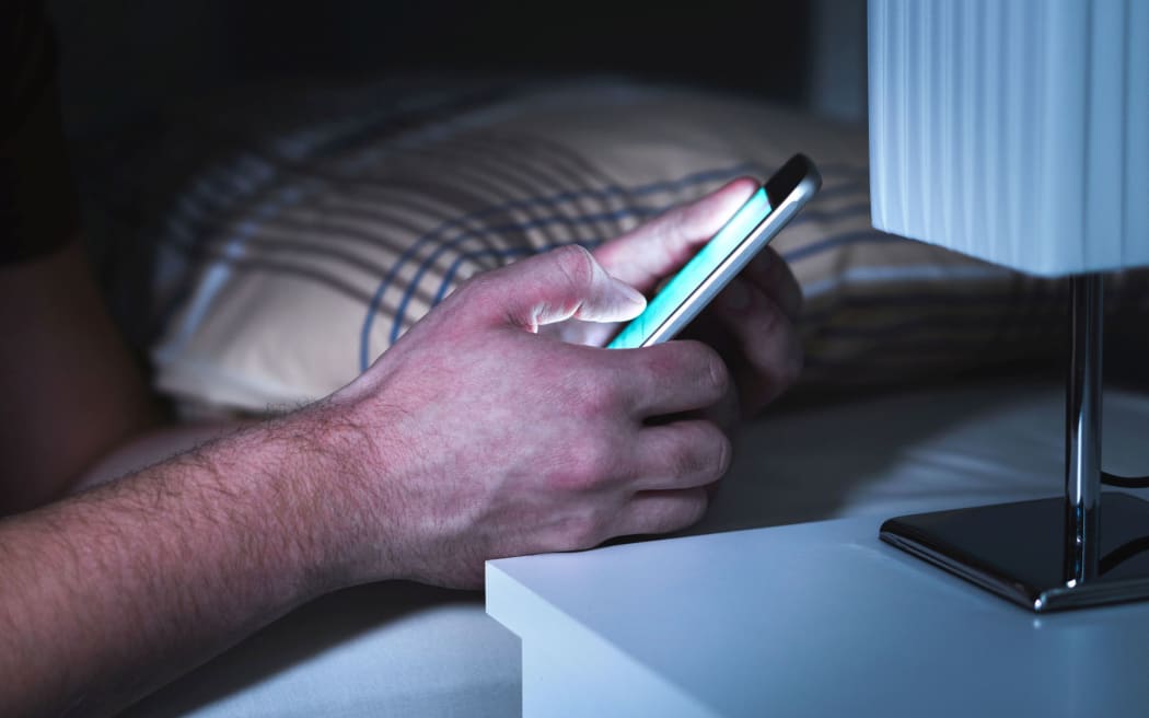 Man using smartphone in bed late, in the middle of the night custom crop