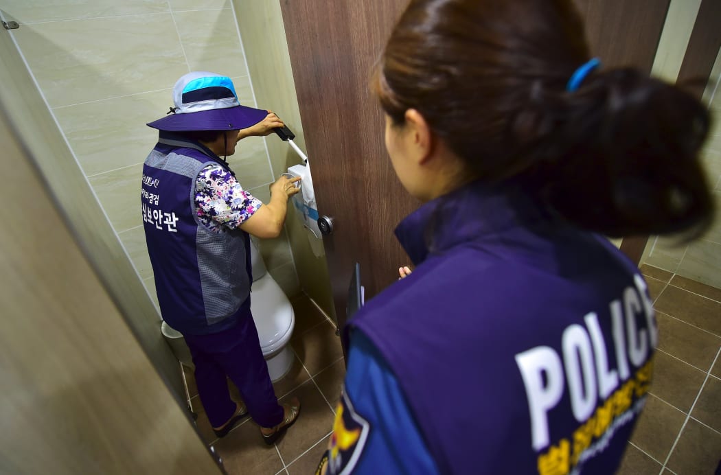 This picture taken on August 18, 2016 shows a member of Seoul city's "hidden camera-hunting" squad (L) and a policewoman (R) inspecting a women's bathroom stall to find "secret camera" at a museum in Seoul.