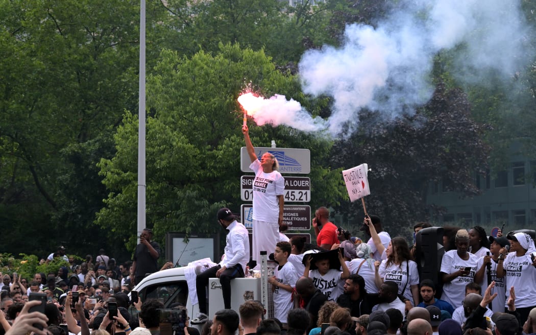 Mounia, the mother of Nahel, a teenage driver shot dead by a policeman, waves a light flare as she stands atop a truck during a commemoration march for her son, in the Parisian suburb of Nanterre, on June 29, 2023. Violent protests broke out in France in the early hours of June 29, 2023, as anger grows over the police killing of a teenager, with security forces arresting 150 people in the chaos that saw balaclava-clad protesters burning cars and setting off fireworks. Nahel M., 17, was shot in the chest at point-blank range in Nanterre in the morning of June 27, 2023, in an incident that has reignited debate in France about police tactics long criticised by rights groups over the treatment of people in low-income suburbs, particularly ethnic minorities. (Photo by Alain JOCARD / AFP)