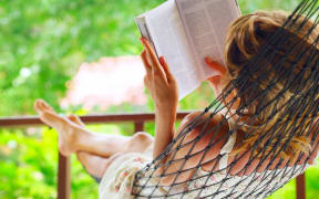 9912221 - young woman lying in hammock in a garden and reading a book. shallow dof. focus on a left shoulder
