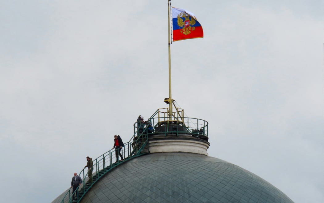 People gather on the dome of the Senate Palace -- topped with the Russian flag -- which is one of the main buildings within the Kremlin compound, in central Moscow on May 3, 2023. - Russia said on May 3, 2023 it had shot down two drones aimed at President Vladimir Putin's Kremlin residence in what it called a Ukrainian "terrorist" assassination attempt.