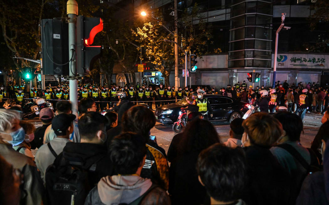 People gather as police officers block Wulumuqi street, in Shanghai on 27 November, 2022, in the area where protests against China's zero-Covid policy took place the night before following a deadly fire in Urumqi, the capital of the Xinjiang region.
