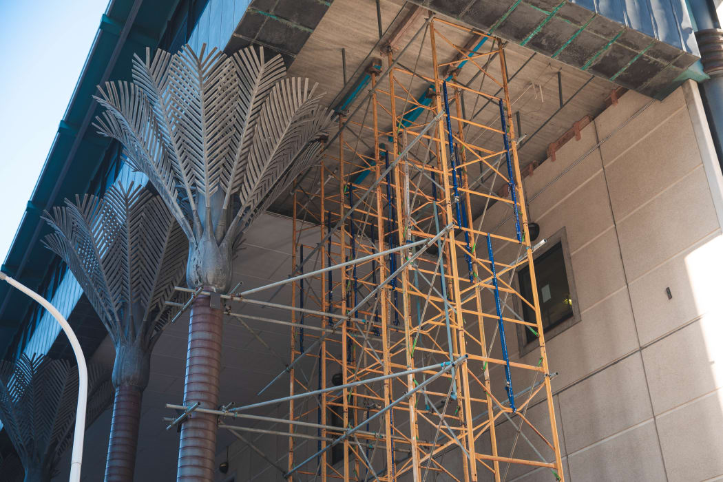 Scaffolding by the metal nikau sculptures of the Wellington Central Library building.