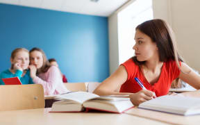 A photo of a girl who is turning around in the classroom to look at two other girls who have been gossiping about her.
