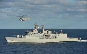 The HMNZS Te Kaha out at sea with a helicopter flying above