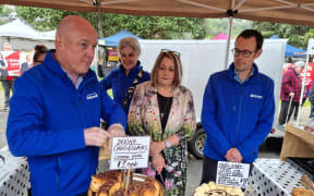 National leader Christopher Luxon serving up some pastries at the River Markets in Whanganui, he is with National's Whanganui candidate Carl Bates (right) and Te Tai Hauauru candidate Harete Hipango (second left), but Labour's Whanganui MP Steph Lewis (third left) is also in shot.