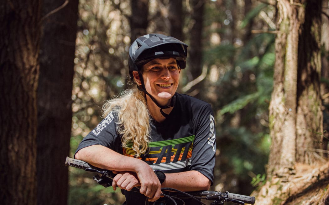 New Zealand mountain bike racer Kate Weatherly leans on her bike, smiling.