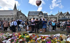 A group of students sing in front of flowers left in tribute to victims of Friday's attacks at the Botanical Garden in Christchurch.