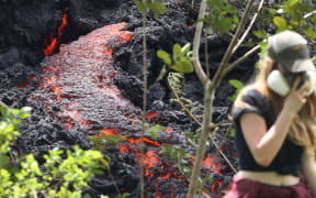 Lava flows at a new fissure in the aftermath of eruptions from the Kilauea volcano on Hawaii's Big Island as a local resident walks nearby after taking photos.