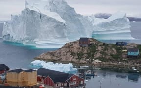 An iceberg behind houses and buildings after it grounded outside the village of Innarsuit, an island settlement in the Avannaata municipality in northwestern Greenland.