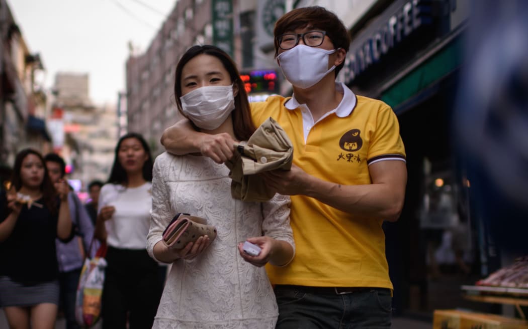 A couple wearing face masks walk on a street in the popular student area of Hongdae in Seoul.