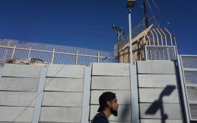 A pedestrian walks towards the port of Entry at the US-Mexico border wall.