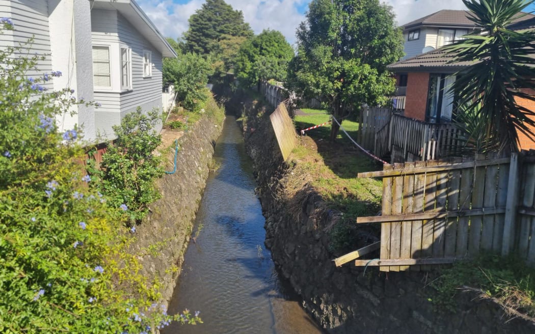 A broken fence is seen alongside a waterway in Mt Roskill after the Auckland floods of January 2023.