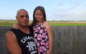 Marcus Walsh, 42, with Kayla Tom, 8, beside their back fence which looks out on to Ohakea Air Force base where the contamination originated.