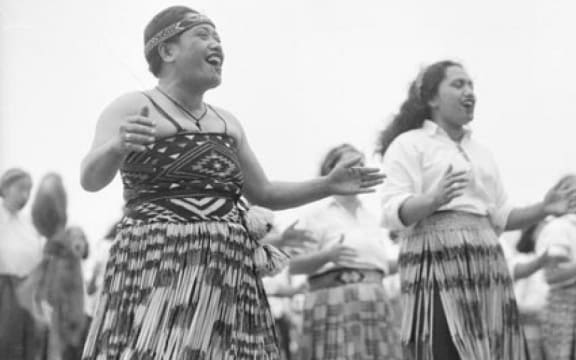 Māori wahine wearing piupiu (skirts) smile while performing a waiata.