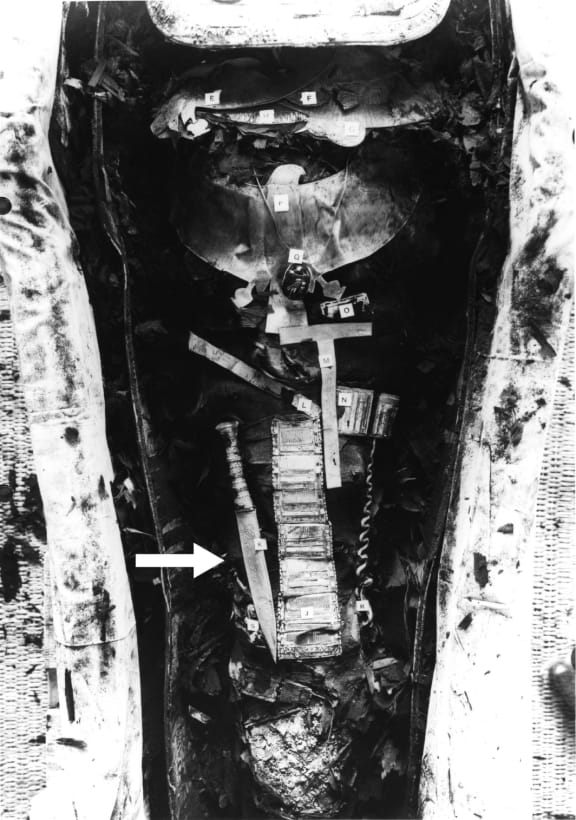 A black and white picture of the Tutankhamun mummy, showing the iron dagger (34.2 cm long) placed on the right thigh (arrowed).