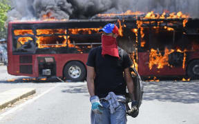 An opposition demonstrator walks near a bus in flames during clashes with soldiers loyal to Venezuelan President Nicolas Maduro near La Carlota military base in Caracas.