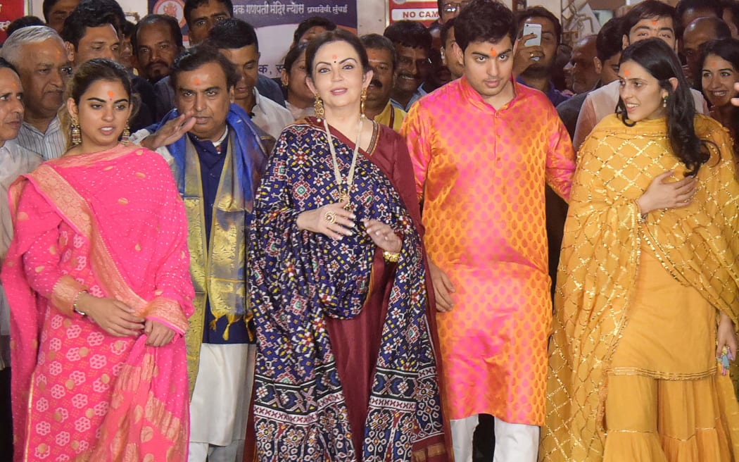 This picture taken on March 25, 2018 shows Indian business magnate chairman, managing director and largest shareholder of Reliance Industries Limited Mukesh Ambani (2L) and his wife Nita Ambani (C) along with their children Isha Ambani (L), Akash Ambani (3R), Anant Ambani (R) and Akash's fiancée Shloka Mehta (2R) posing for a photograph after seeking blessings at the Siddhivinayak temple in Mumbai. (Photo by AFP)