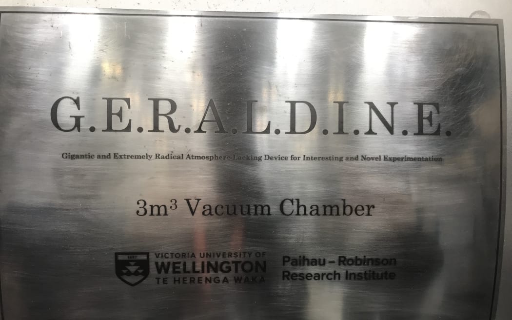 A close up of a metallic surface with the words 'G.E.R.A.L.D.I.N.E. Gigantic and Extremely Radical Atmosphere-Lacking Device for Interesting and Novel Experimentation. 3m3 vaccum chamber. Victoria University of Wellington Te Herenga Waka Paihau Robinson Reserach Institute.'