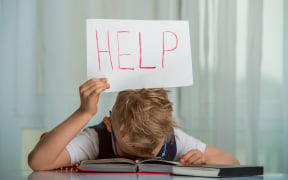 Kid boy sleeping with a textbook over his head and holding a sign with the word Help