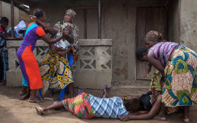 Women faint while volunteers take away the body of a woman who died of Ebola in Sierra Leone.