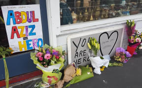 Floral tributes and signs are building up outside the shop of Abdul Aziz, who threw an eftpos machine at the attacker.