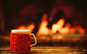 Cup of hot drink in front of warm fireplace.