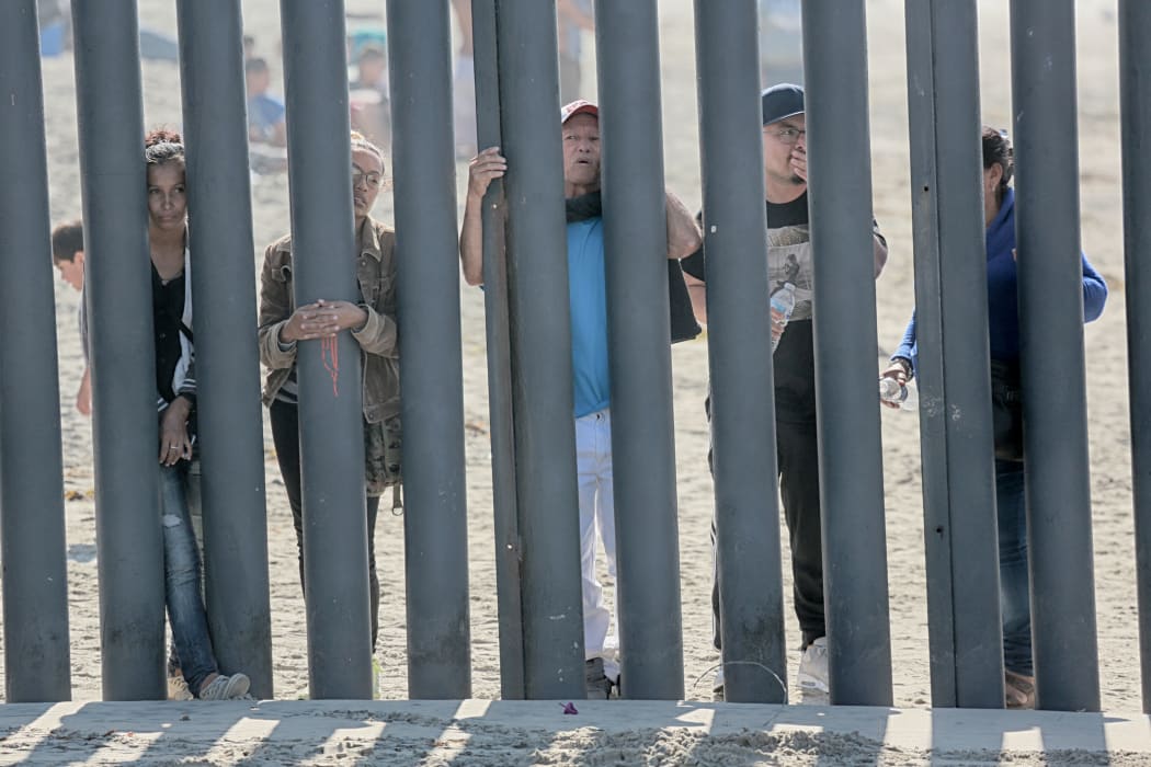 Honduran caravan members look through through the fence at the US-Mexico border wall in San Ysidro on November 18, 2018.