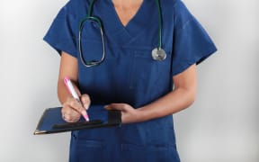Doctor with a stethoscope writing on a clipboard.