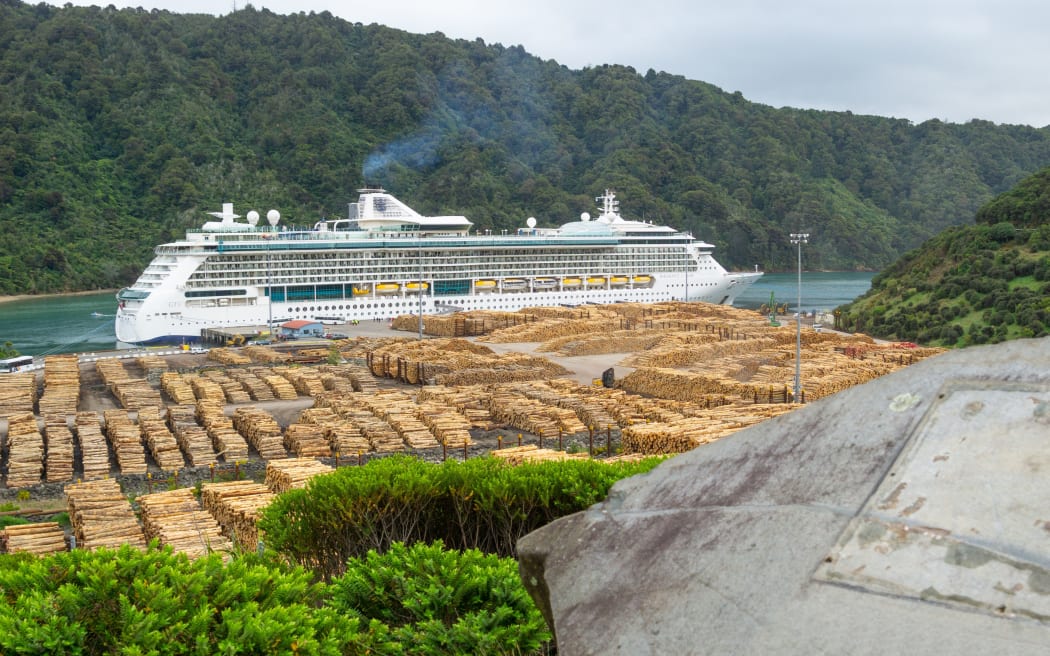 PICTON NEW ZEALAND- OCTOBER 2 2018; Radiance of Seas huge passenger cruise ship moored at Shakespeares Bay Wharf with logs stcked and waiting to be shipped.