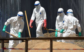 Health workers from the Liberian Red Cross shovel sand to absorb fluids from the bodies of Ebola victims in Monrovia.