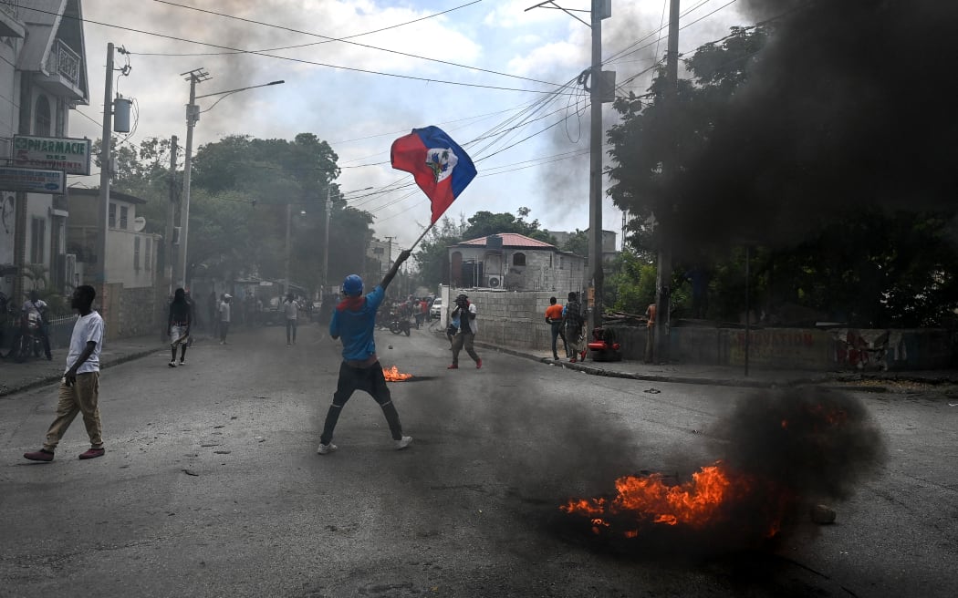 A man holds a Haitian flag as a tire burns during a demonstration against insecurity in Carrefour-Feuilles, a district of Port-au-Prince, Haiti, on August 14, 2023. (Photo by Richard PIERRIN / AFP)