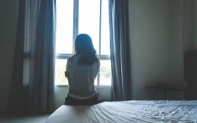 woman sitting on bed in room with light from window (abuse concept)