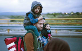 A refugee carries a child as he walks to board a bus after crossing the Greek-Macedonian border.