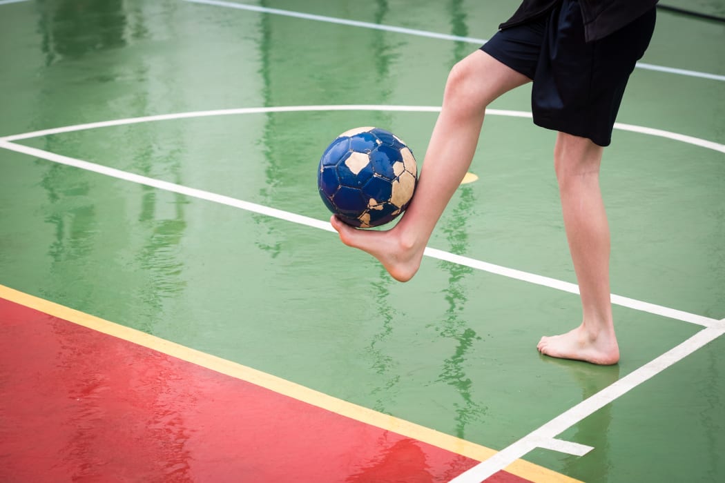 Barefoot boy playing football on a wet sports court.