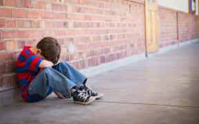 Sad pupil sitting alone in corridor at the elementary school