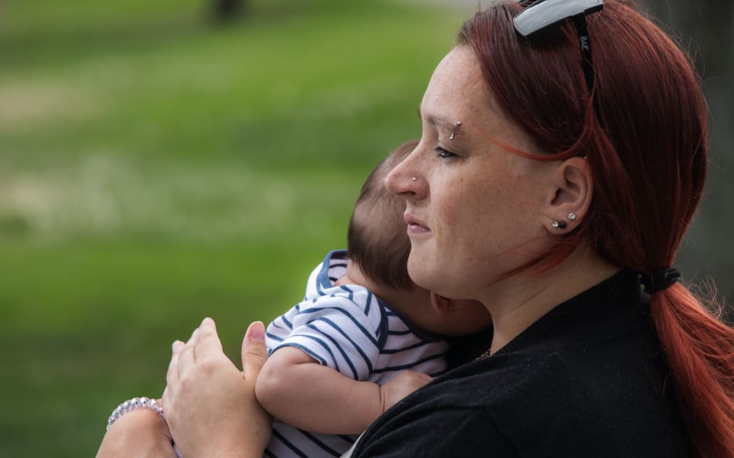 Mariska Kruger sits on a park bench in Napier holding her youngest son.