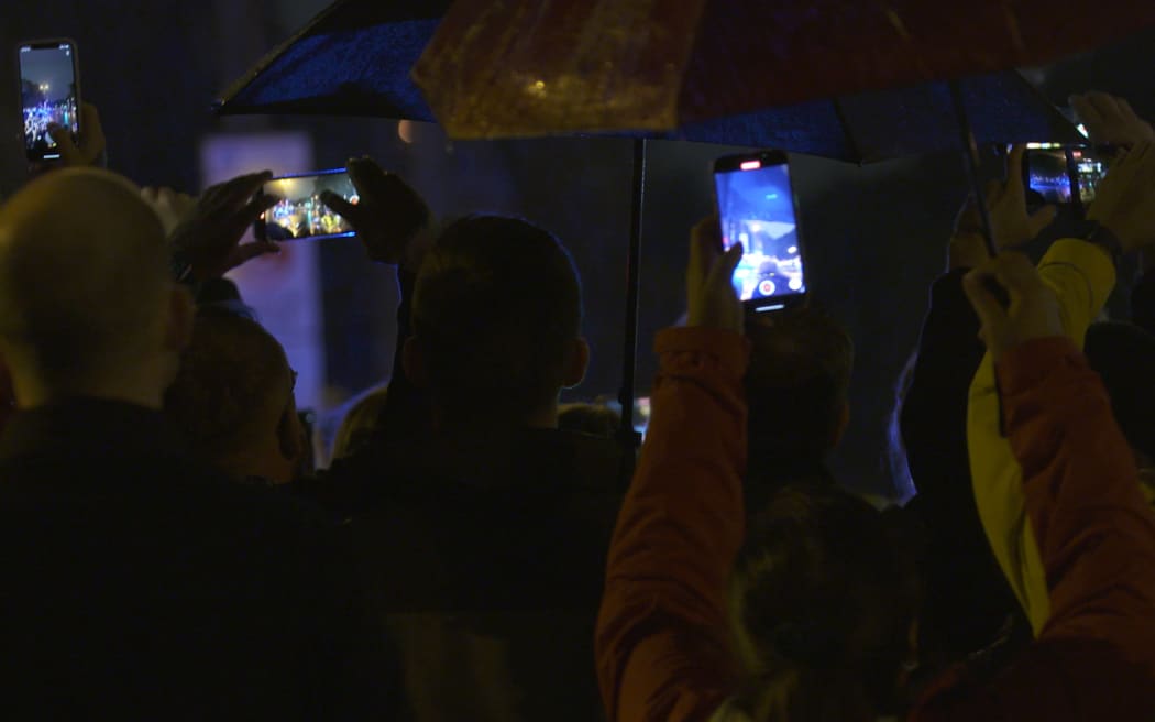 By dark and rain, keen commemorations try to grab a picture of the Queen’s Hearse en route to Buckingham Palace.