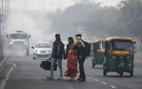 People cross a street as motorists drive past amid smoggy conditions in New Delhi on November 15, 2020. (Photo by Prakash SINGH / AFP)