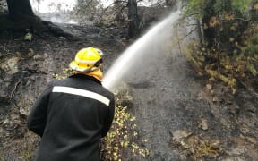 A firefighter dampens down a hot spot in the wake of the devastating Port Hills fires.