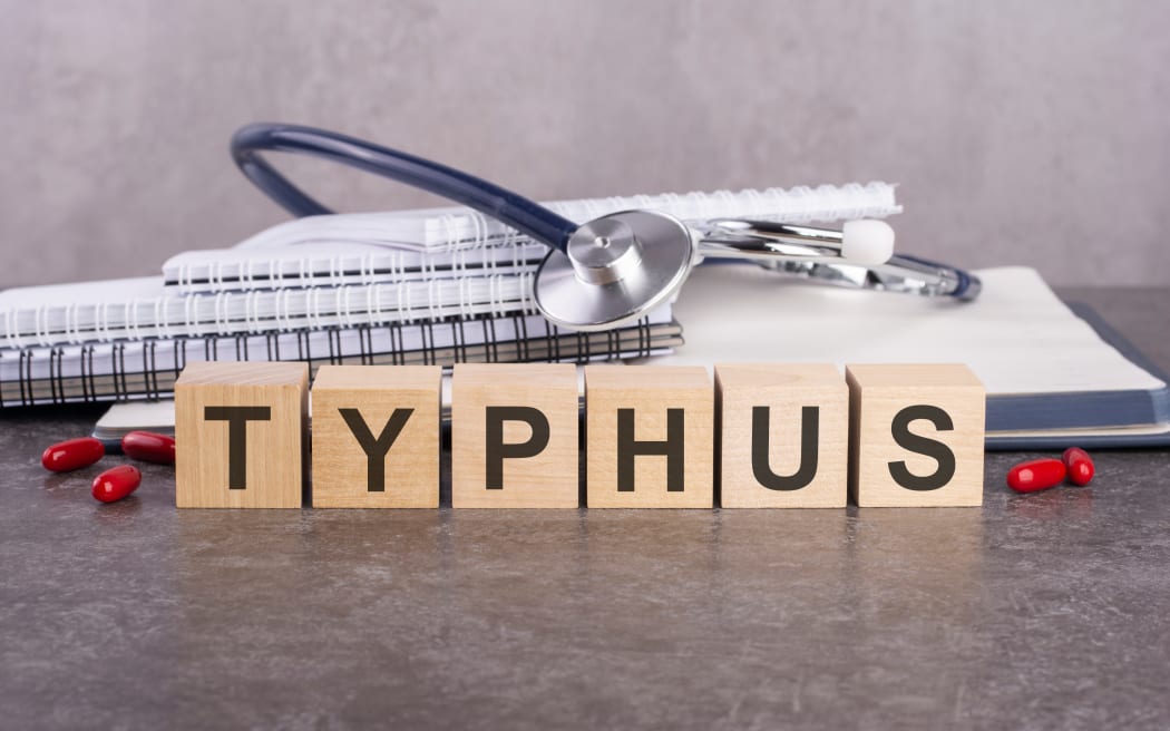 TYPHUS - text is made up of wooden blocks standing on a gray table. In the background is a stack of paper notebooks for writing and tablets. medical concept, gray background