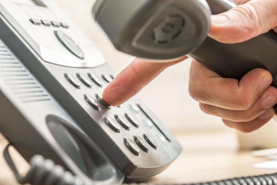 A close-up of a man's hand dialing numbers on a landline phone
