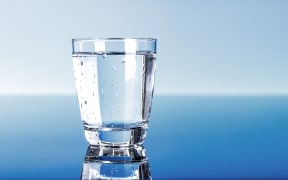 A close-up of a glass of drinking water, on a blue background