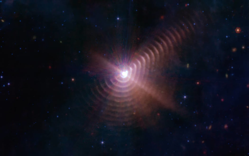 Las dos estrellas en Wolf-Rayet 140 producen capas de polvo cada ocho años que parecen anillos, como se ve en esta imagen del Telescopio Espacial James Webb de la NASA.  Cada anillo se creó cuando las estrellas se acercaron entre sí y sus vientos estelares chocaron, comprimiendo gas y formando polvo.