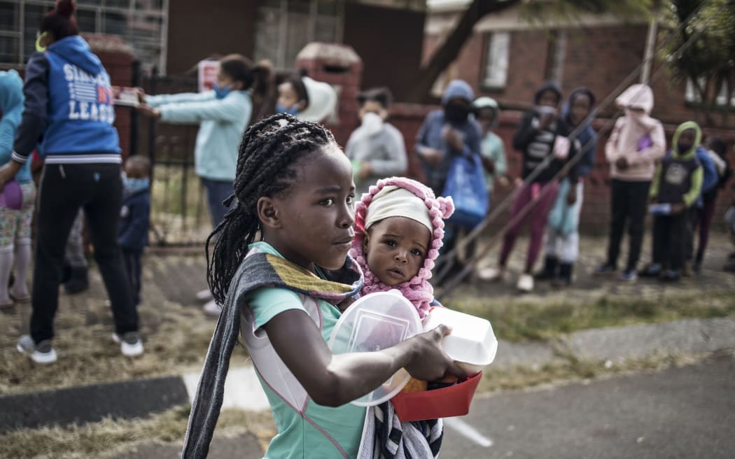 A child holds a sibling while carrying a food parcel received from the grassroots charity Hunger has no Religion in Johannesburg, on May 25, 2020  (Photo by MARCO LONGARI / AFP)
