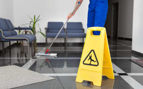 A worker mops a floor next to a 'cleaning in progress' sign.