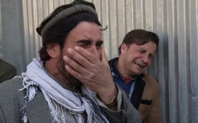 Two Afghan man cry for their relatives outside the Kabul hospital where gunmen dressed as doctors killed more than 30 people.
