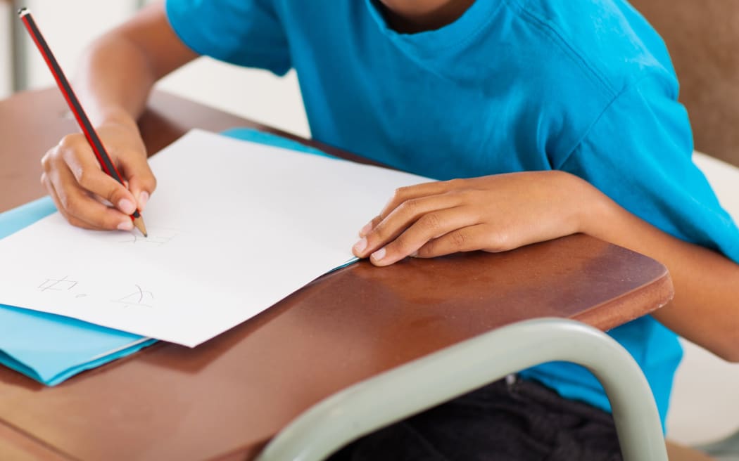 Un jeune garçon écrit sur un bureau dans une école primaire.