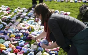 A protester lays out some of the more than 13,000 booties specially knitted for the display.