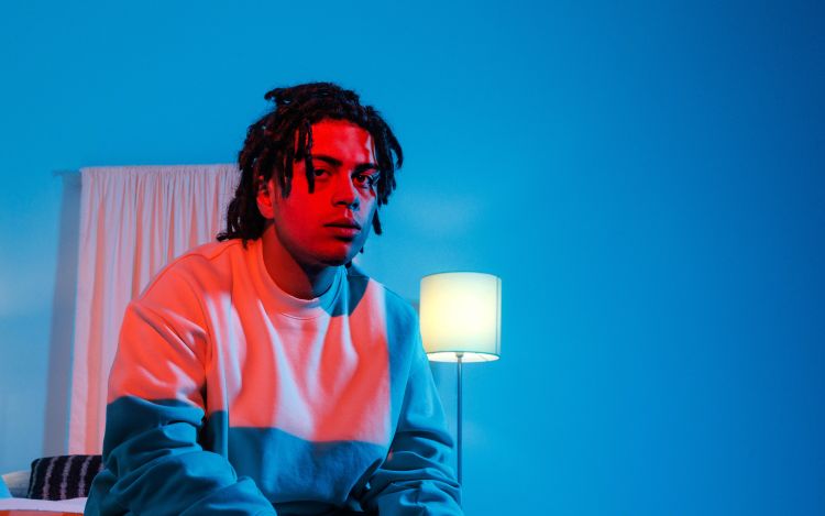 Denzel sitting at the end of a bed in a fluorescent blue and red room